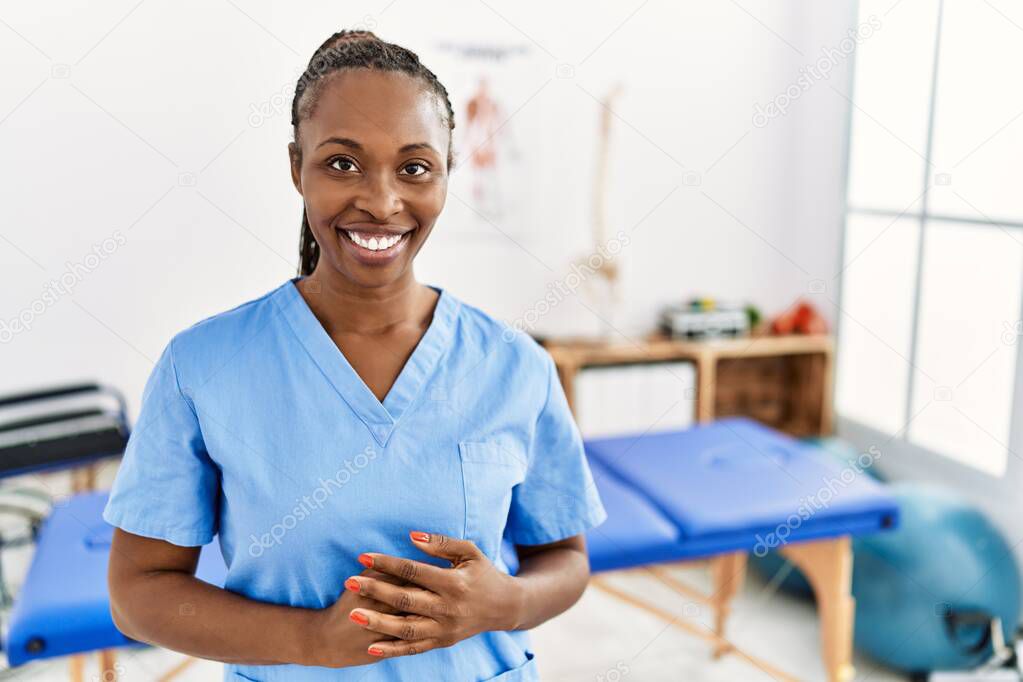 Black woman with braids working at pain recovery clinic with hands together and crossed fingers smiling relaxed and cheerful. success and optimistic 