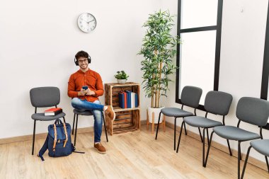 Genç İspanyol adam, bekleme odasında müzik dinlerken kendinden emin bir şekilde gülümsüyor.