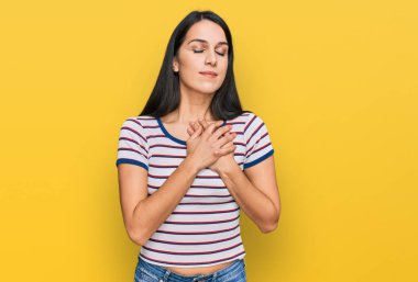 Sıradan çizgili tişört giyen genç İspanyol kız elleri göğsünde, gözleri kapalı ve yüzünde minnet dolu bir jest ile gülümsüyor. sağlık kavramı. 