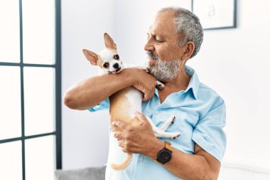 Yaşlı, gri saçlı, gülümseyen ve elinde Chihuahua tutan adam.