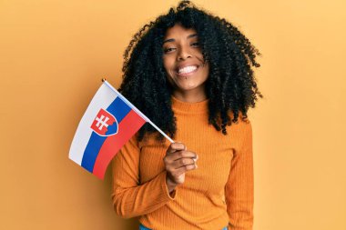 Afro saçlı, Slovakya bayrağı tutan Afro-Amerikalı kadın pozitif ve mutlu görünüyor ve kendine güvenen bir gülümsemeyle dişlerini gösteriyor. 