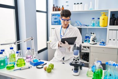 Laboratuvarda panoya yazı yazan, bilim adamı üniforması giyen İspanyol bir genç.