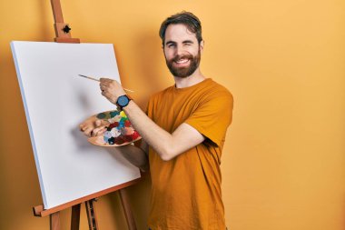 Beyaz, sakallı bir adam boyacı sehpası çizerek ayakta duruyor. Seksi bir ifadeyle kameraya bakıyor. Neşeli ve mutlu bir yüzü var.. 