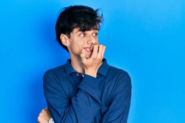 Yakışıklı hippi genç adam mavi arka planda mahsur kalmış stresli ve gergin görünüyor elleri ağız ısıran tırnaklarla. anksiyete. 