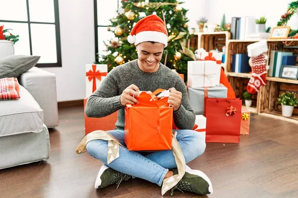 Joven Hombre Hispano Desempacando Regalo Sentado Junto Árbol Navidad Casa —  Fotos de Stock