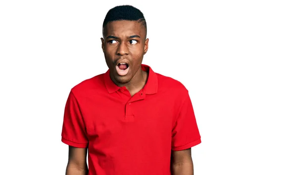 カジュアルな赤いTシャツを着た若いアフリカ系アメリカ人の男性が怒りと怒りで叫んで フラストレーションと激怒叫んで怒っています 怒りと攻撃的な考え方 — ストック写真