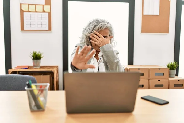 中年女商人坐在办公桌上 在办公室里用手提电脑用手捂住眼睛 用悲伤和恐惧的表情做着停下来的手势 尴尬和消极的概念 — 图库照片