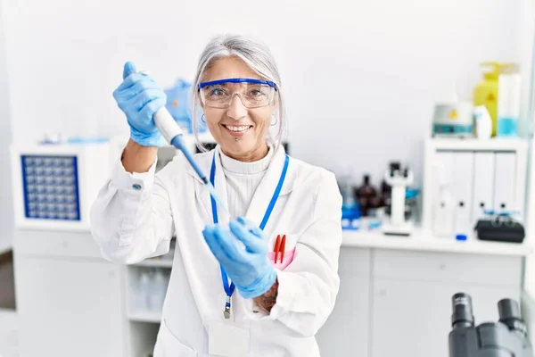 实验室里穿着科学家制服的中年灰发女人用吸管 — 图库照片