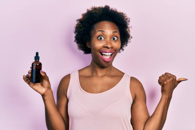 Yüz serumu takmış genç Afro-Amerikalı bir kadın baş parmağını yukarı kaldırıyor ve ağzı açık gülümsüyor. 