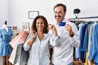 İspanyol orta yaşlı çift ellerinde alışveriş poşetleri ve kredi kartı ile gülümsüyor ve elleriyle küçük boy işaretler yaparak kameraya bakıyor. ölçüm kavramı. 