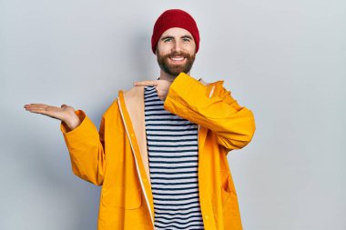 Sarı yağmurluk giyen, sakallı, beyaz bir adam kameraya hayret ediyor ve gülümsüyor.. 