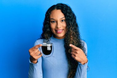 Kahvesini tutan genç Latin kadın gülümsüyor mutlu bir şekilde elini ve parmağını gösteriyor. 