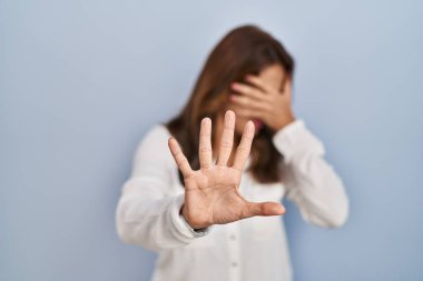İspanyol kadın izole edilmiş arka planda duruyor. Gözlerini ellerle kapatıyor ve üzgün ve korku ifadeleriyle jestleri durduruyor. utangaç ve olumsuz kavram. 
