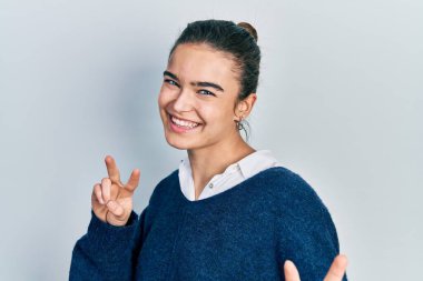 Gündelik giysiler giymiş genç beyaz kız kameraya bakıp zafer işareti yapıyor. İki numara.. 