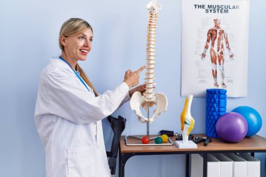 Fizyoterapi kliniğindeki omurganın anatomik modelini gösteren fizyoterpist üniforma giyen genç sarışın kadın.