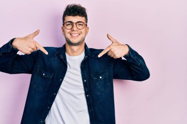 Gündelik kıyafetler ve gözlük takan, kendine güvenen, gülümseyen, kendini gururlu ve mutlu gösteren İspanyol genç bir adam.. 