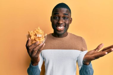 Genç Afro-Amerikan adam elinde kaseyle pişmemiş spagetti ile başarıyı mutlu bir gülümsemeyle ve kazanan yüz ifadesiyle kutluyor. 