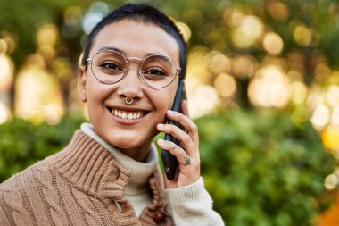 Kısa saçlı, gülümseyen, telefonda konuşan genç İspanyol kadın.