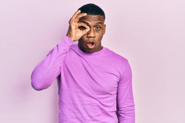 Sıradan pembe kazak giyen genç siyah bir adam şaşırmış yüz ifadesiyle şok olmuş, parmaklarından bakan gözler. İnançsız ifade. 
