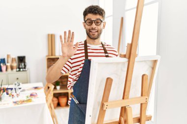 Sanat stüdyosundaki Arap genç adam merhaba diyor mutlu, güler yüzlü, dostça karşılama jesti. 