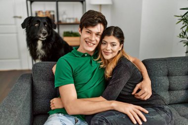 Genç, beyaz bir çift, mutlu bir şekilde gülümsüyor ve evde köpekleriyle koltukta oturuyor..