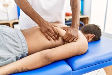 İki erkek fizyoterapist ve hasta klinikte rehabilitasyon seansı yapıyorlar.