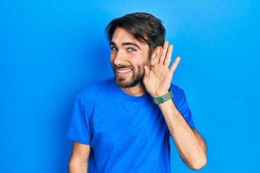 Gündelik kıyafetler giyen, ağzı kulaklarında gülümseyen genç İspanyol bir adam dedikoduları ve dedikoduları dinliyor. Sağırlık kavramı. 