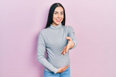 Mavi gözlü güzel bir kadın bebek bekliyor, hamile karnına dokunuyor mutlu bir şekilde gülümsüyor avuç içi yardım ve kabullenme eli uzatıyor.. 