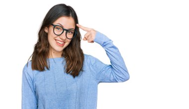 Gündelik kıyafetler ve gözlük takan genç ve güzel bir kadın gülümseyerek tek parmağıyla kafasını işaret ediyor, harika bir fikir ya da düşünce, iyi bir hafıza. 