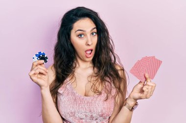 Poker oynayan genç İspanyol kadın elinde iskambil fişleri ve kartlarıyla şaşkın, şüpheci ve alaycı görünüyor, ağzı açık kalmış. 