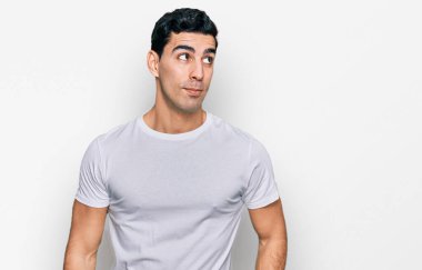 Yakışıklı, beyaz tişörtlü, yakışıklı bir adam. Gülümsüyor, yan tarafa bakıyor ve düşünüyor.. 