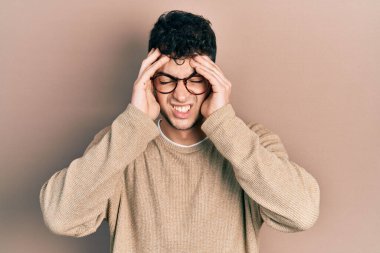 Gündelik kıyafetler giyen ve eli kafasında gözlük takan genç bir İspanyol, stres yüzünden baş ağrısı çekiyor. migren ağrısı. 