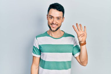 İspanyol asıllı genç adam, gündelik giysiler giyip dört numarayı gösterip işaret ederken kendinden emin ve mutlu bir şekilde gülümsüyor.. 
