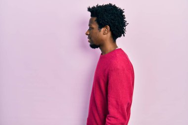 Afro-Amerikalı genç bir adam günlük giysiler giymiş, rahat bir görünüm takınıyor, doğal bir yüzü ve kendine güvenen bir gülümsemesi var.. 