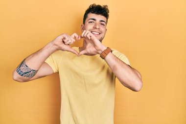 Gündelik tişört giyen, aşık gülümseyen, elleriyle kalp sembolü yapan genç bir İspanyol. romantik kavram. 