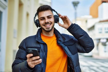 Yakışıklı, sakallı, neşeli, kendine güvenen, kışlık palto giyen, akıllı telefondan müzik dinleyen bir İspanyol.