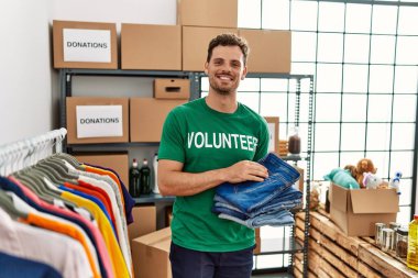 Yardım merkezinde katlanmış kot tutan gönüllü üniformalı bir İspanyol genç.