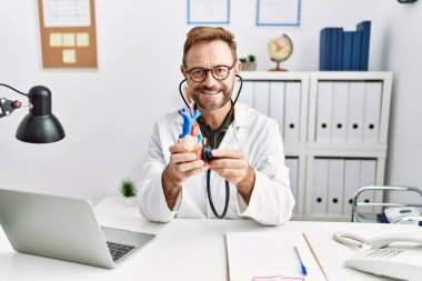 Orta yaşlı İspanyol adam doktor üniforması giyiyor. Klinikte kalp bakımı yapıyor.