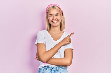 Güzel, beyaz tişört giyen, yüzünde kocaman bir gülümseme olan, eli ve parmağı kameraya bakan sarışın bir kadın.. 