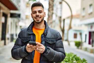 Yakışıklı, sakallı, mutlu ve kendine güvenen, akıllı telefon kullanan, kışlık palto giyen bir İspanyol.