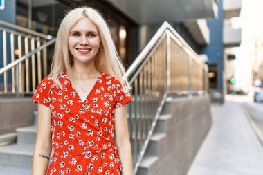 Genç sarışın kız gülümsüyor, mutlu bir şekilde şehirde duruyor..