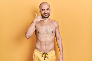 Mayo giyen genç kel adam gülümsüyor telefonla el ve parmaklarıyla jest yapıyor telefonda konuşuyor gibi. iletişim kavramları. 