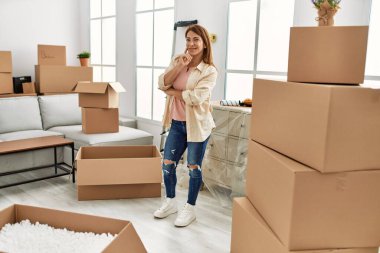 Orta yaşlı, beyaz bir kadın yeni evinde mutlu bir şekilde gülümsüyor..