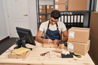 Latin kökenli genç bir iş adamı iş yerinde paket üzerine yazıyor.