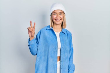 Güzel sarışın kadın yün şapka takıyor ve parmaklarını iki numara ile göstererek gülümsüyor. Kendinden emin ve mutlu.. 