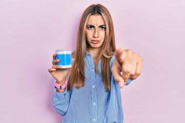 Kulak kiri temizleyiciler tutan güzel İspanyol kadın kamerayı işaret ediyor ve kendine güvenen sen ciddi görünüyorsun. 