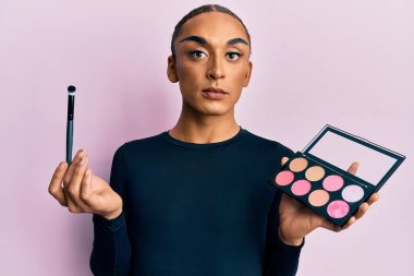 Makyaj yapan, elinde makyaj fırçası tutan, yüzünde ciddi bir ifadeyle rahatlamış, uzun saçlı İspanyol bir adam. Basit ve doğal bir şekilde kameraya bakıyorsun.. 