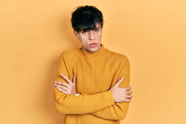 Handsome hipster young man wearing casual yellow sweater shaking and freezing for winter cold with sad and shock expression on face