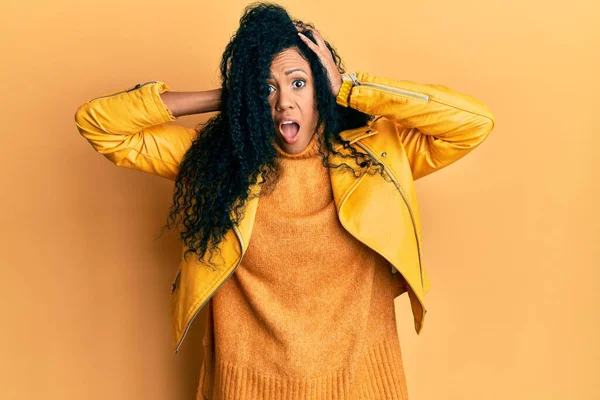 Orta yaşlı Afro-Amerikalı kadın yün kazak ve deri ceket giyiyor. Deli ve elleri başında korkmuş, ağzı açık şoktan korkmuş ve şaşırmış. 
