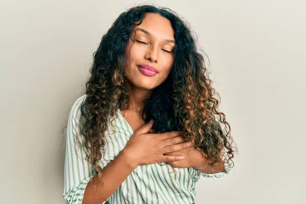 Gündelik kıyafetler giyen genç Latin kadın elleri göğsünde, gözleri kapalı ve yüzünde minnet dolu bir jest ile gülümsüyor. sağlık kavramı. 